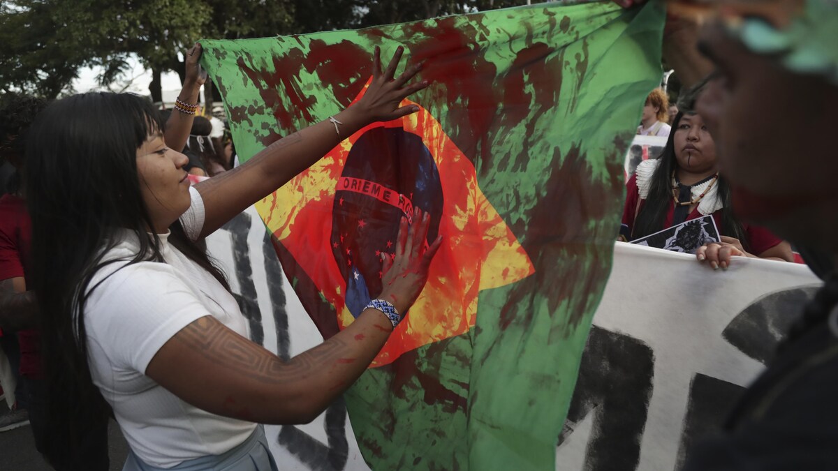 Une manifestants met de la peinture rouge sur le drapeau brésilien