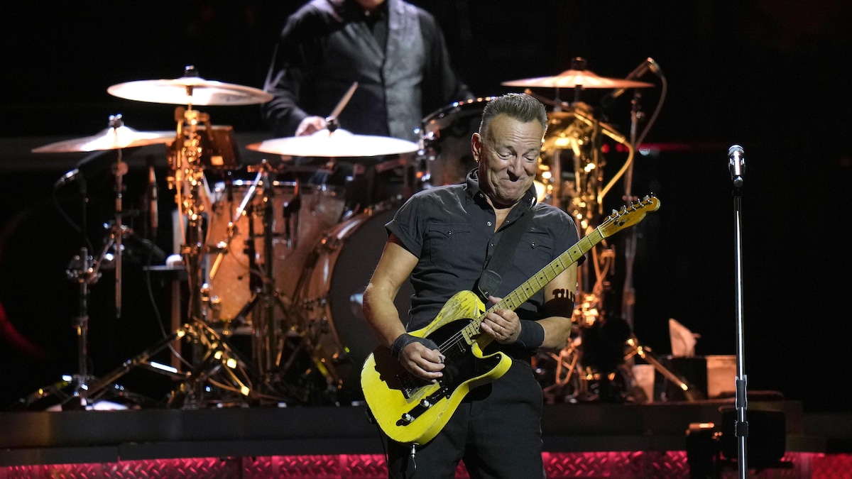 Bruce Springsteen joue de la guitare sur scène. On voit un homme à la batterie derrière lui. 