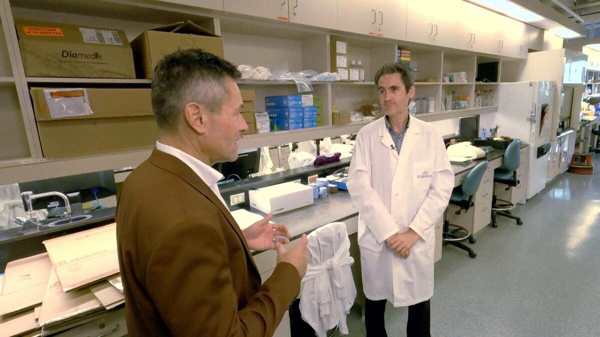 Un homme en veston discute avec un homme en sarrau blanc dans un laboratoire.