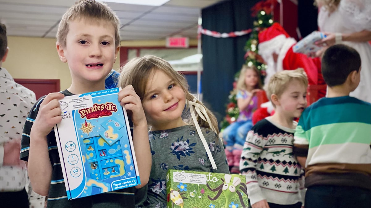 Deux enfants sourient à la caméra, cadeaux à la main.
