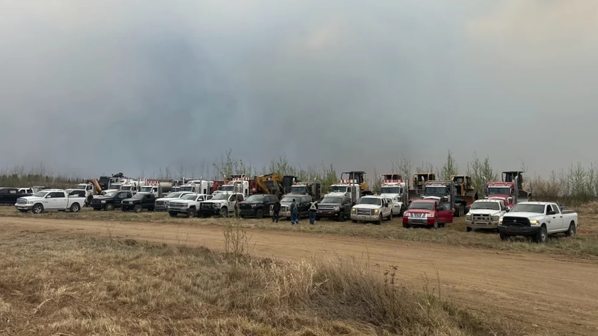 Des camions sont garés devant une route alors que se dégage de la fumée des feux de forêt.