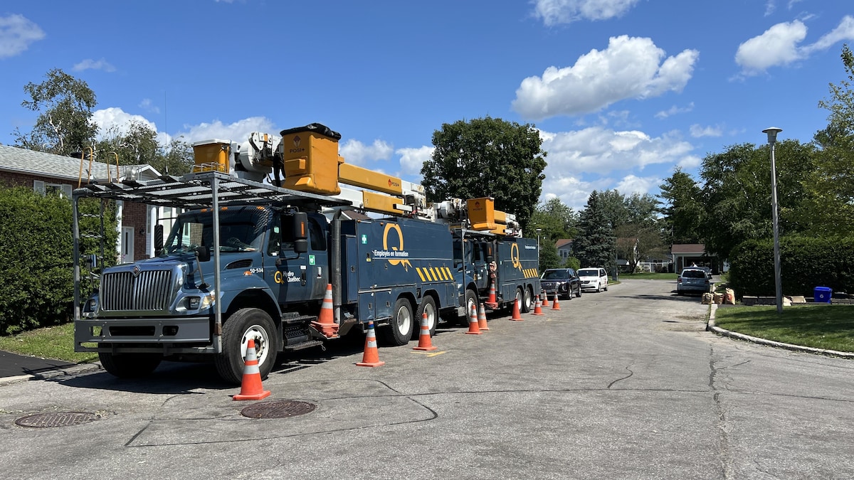 Deux camions d'Hydro-Québec sont stationnés en bordure d'une rue résidentielle, entourés de cônes orange.