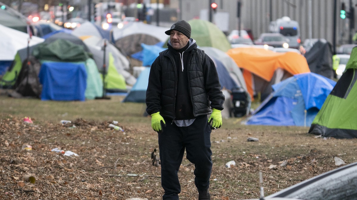 Un homme se tient debout au milieu d'un campement comptant plusieurs tentes.