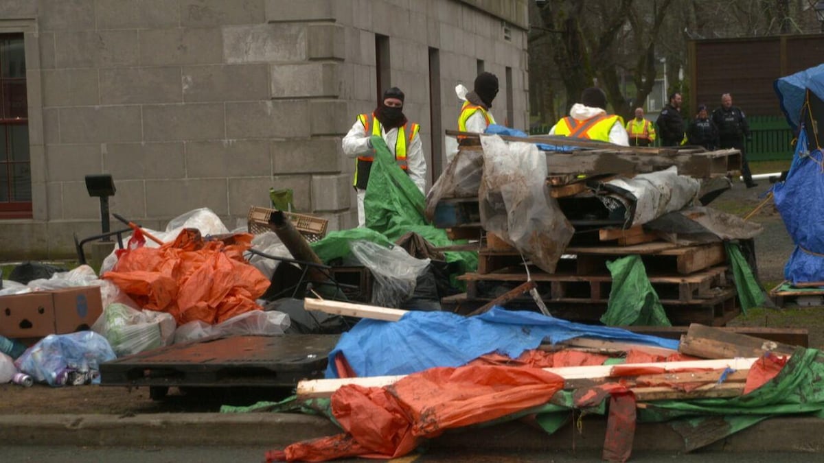 Des travailleurs retirent des tentes, des palettes de bois et d’autres objets d'un campement.