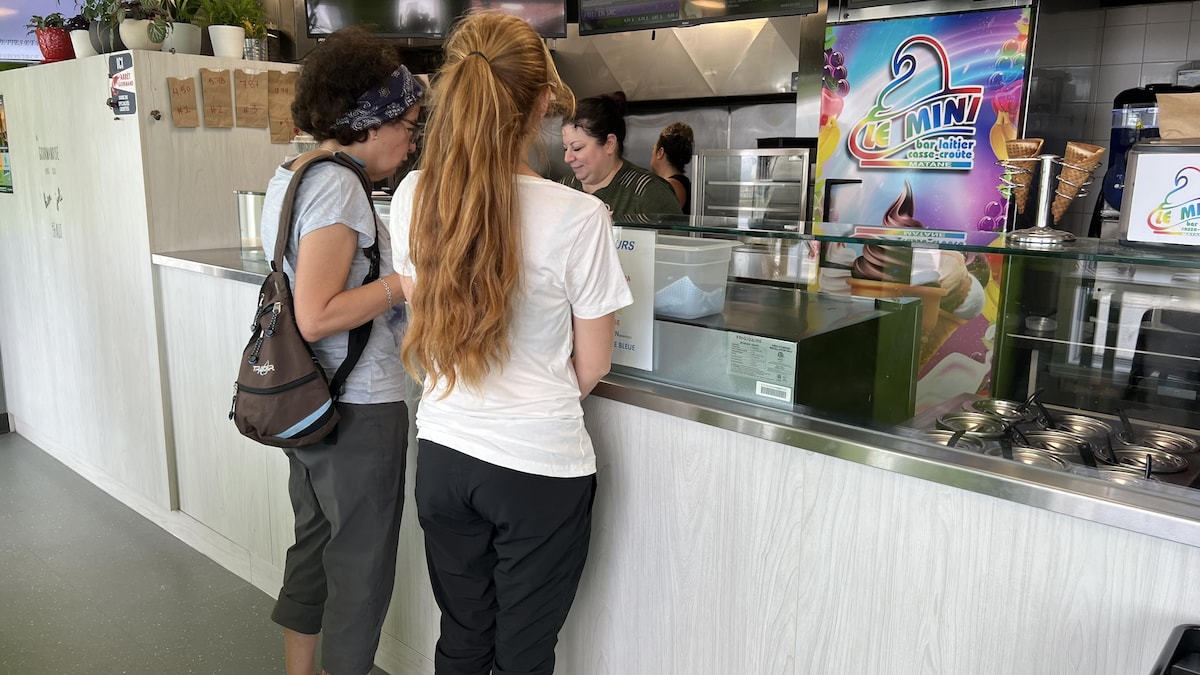 Deux femmes de dos se tiennent devant un comptoir où on sert de la crème glacée.