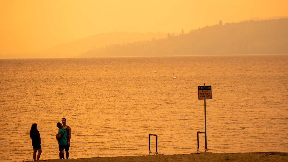 Des gens discutent dans une épaisse fumée sur la plage Boyce-Gyro, sur le bord du lac Okanagan à Kelowna, en Colombie-Britannique, le vendredi 18 août 2023.