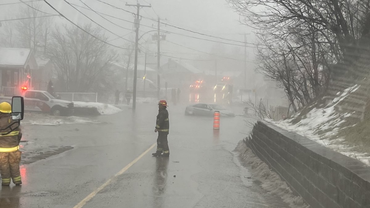 Des pompiers sur une rue inondée où une voiture est immergée.