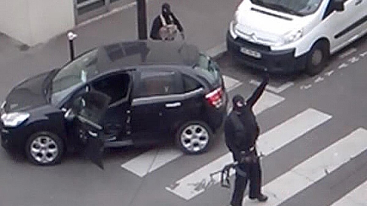 Un homme armé et cagoulé lève le bras dans la rue.