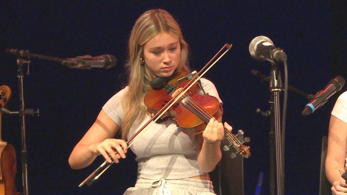 Une adolescente assise joue du violon.