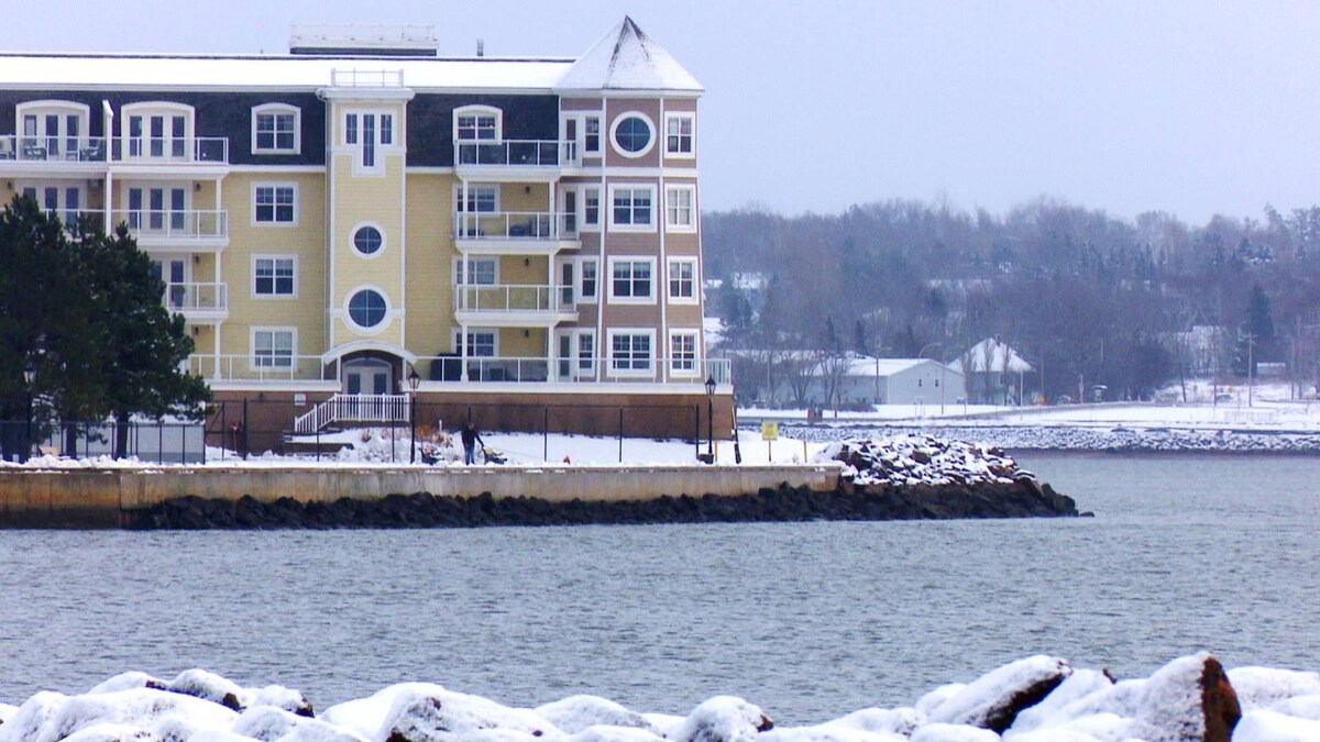 Un édifice jaune de plusieurs étages sur le bord de l'eau, en hiver, photographié de l'autre côté de la rive.