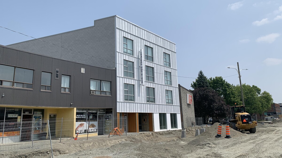 Une nouvelle bâtisse s'élève près d'une épicerie et devant une rue en travaux.