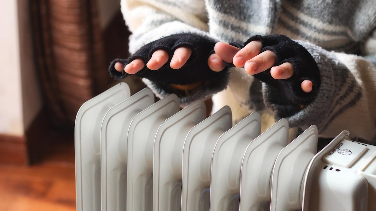 Une femme place ses deux couvertes de gants aux doigts coupés au-dessus d'un radiateur dans un appartement.