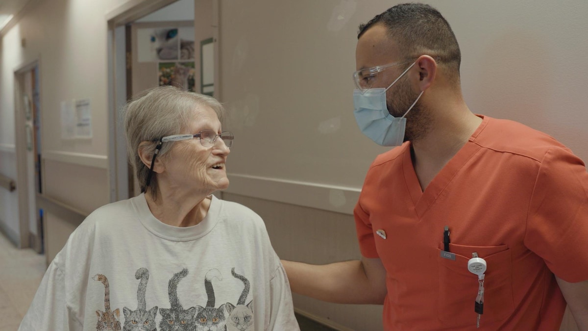 Un infirmier portant un masque accompagne une femme âgée dans un corridor d'un CHSLD.