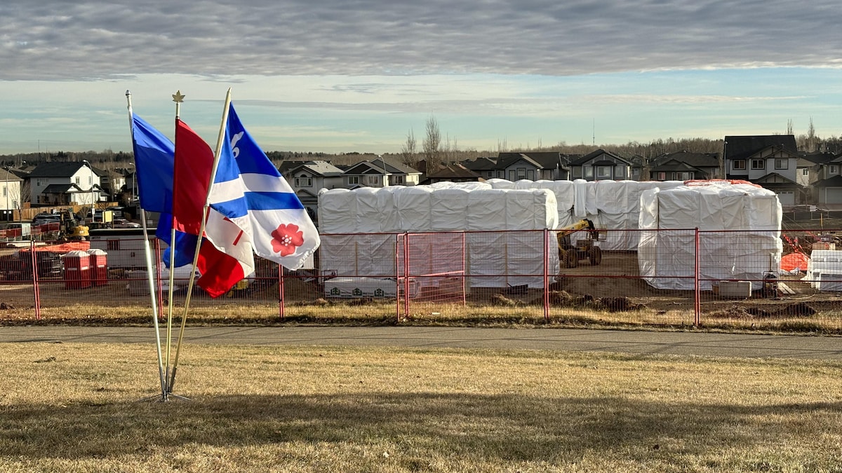 On peut voir les drapeaux canadiens, albertains et franco-albertains devant le chantier de construction du nouveau bâtiment. 