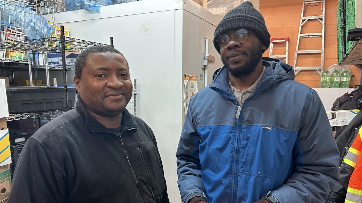 Deux hommes devant des étalages de nourriture non périssable.