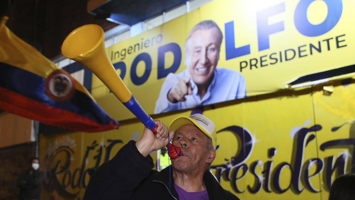 Un homme souffle dans une trompette devant une affiche politique.