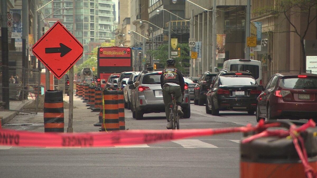 Une partie d'une rue est fermée en raison de la construction, ce qui force les automobilistes et un cycliste de se partager les deux autres voies de circulation.