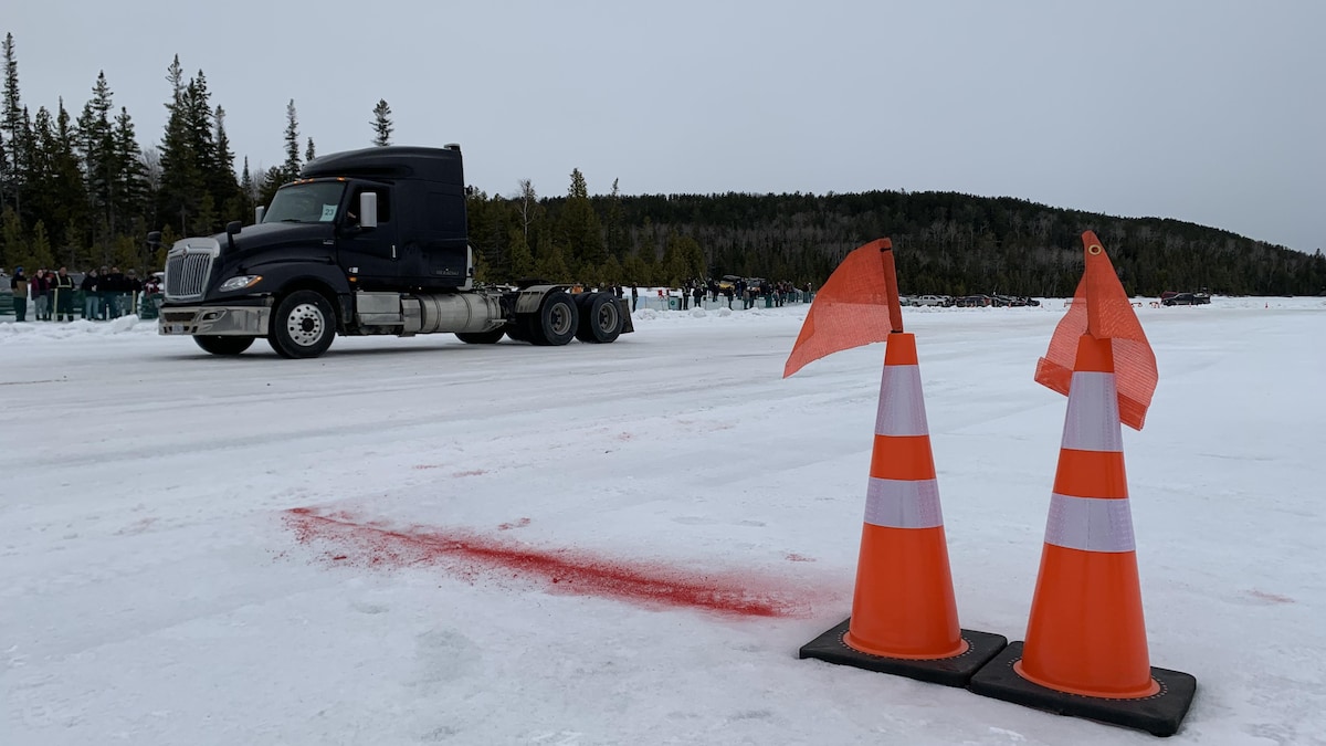Deux cônes orange sont posés sur la neige. Au loin, un camion est stationné.