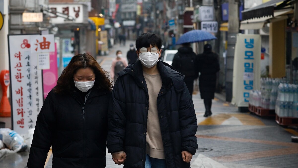 Un couple portant des masques chirurgicaux marche dans une rue.