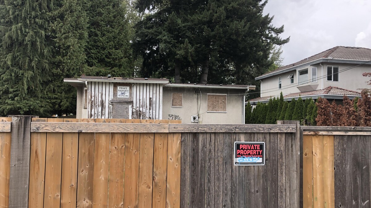 Une maison en abandon derrière une clôture où il y a une affiche expliquant qu'il s'agit d'une propriété privée.