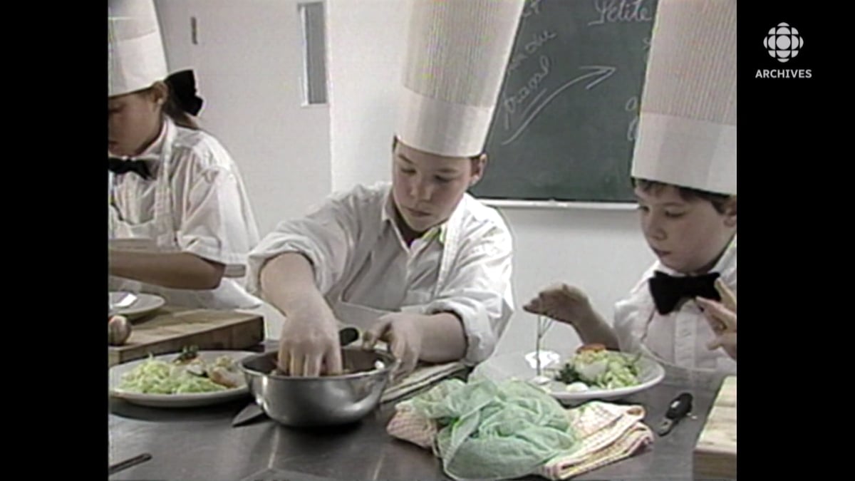 Deux garçons vêtus d'un tablier et d'une toque de chef préparent et disposent des aliments dans des assiettes.