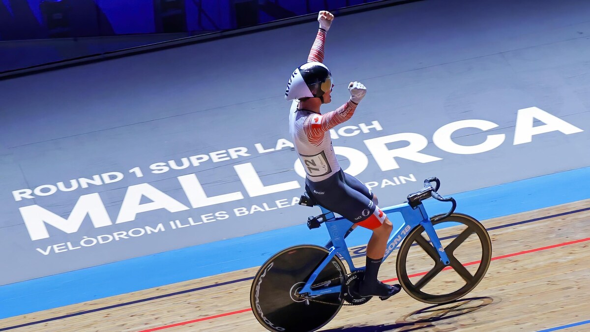Mathias Guillemette, en piste sur son vélo, lève les bras dans les airs en signe de victoire. 