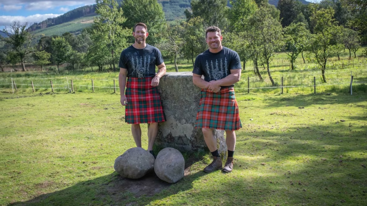 Deux hommes en kilt posent avec de grosses pierres rondes à leurs pieds.