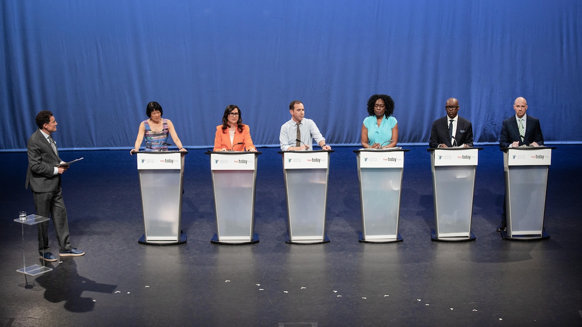 Les six candidats sur scène, derrière des lutrins. À gauche, le modérateur Steve Paikin les regarde.