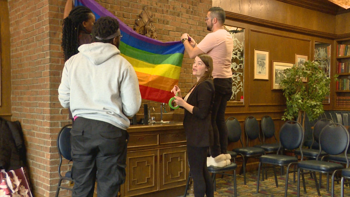 Des personnes hissent le drapeau de la communauté LGBTQ+ dans un espace communautaire en Alberta.