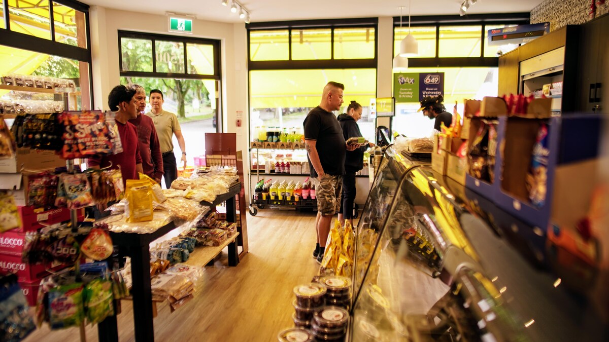 Plusieurs clients sont à la caisse d’une épicerie de quartier, d’autres rentrent dans le magasin.