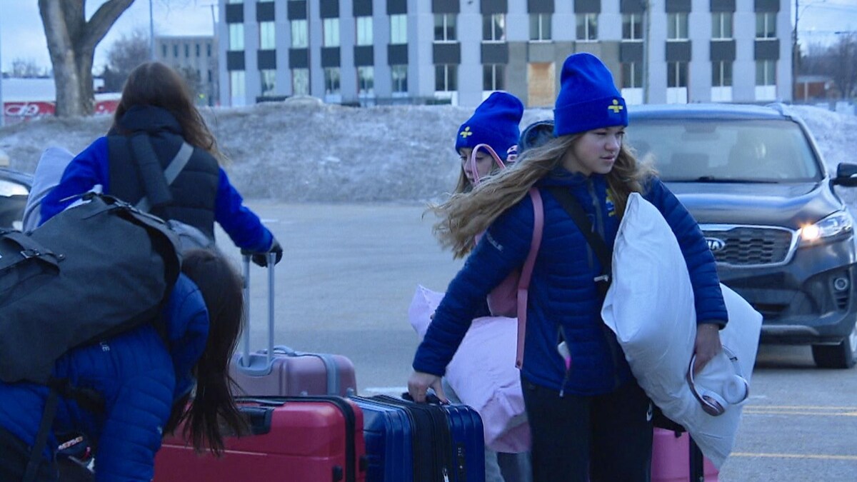Des jeunes filles habillées aux couleurs des Jeux du Québec déplacent leurs valises et leurs oreillers. 