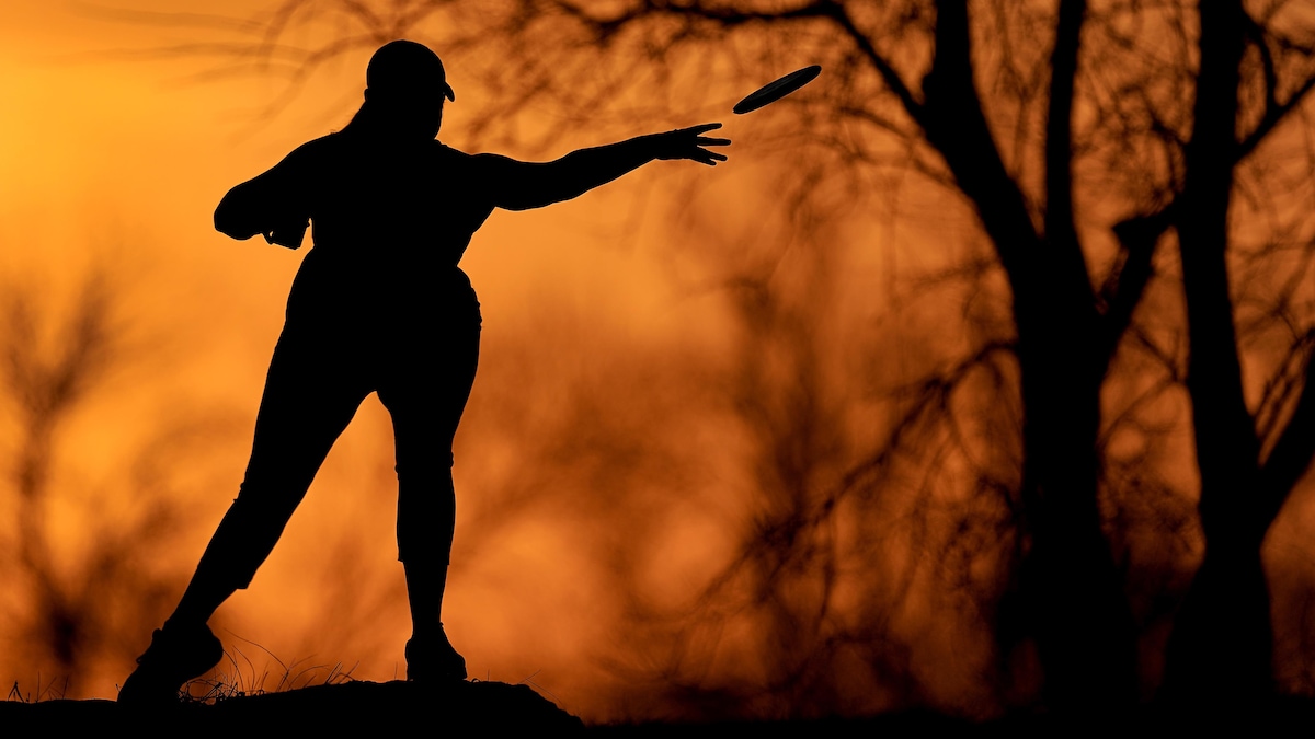 Silhouette d'une femme sur un fond orange. Elle lance un frisbee dans un parc.