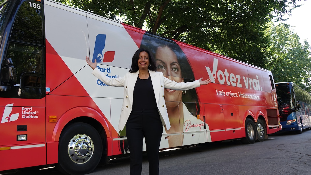 Dominique Anglade écarte les bras en souriant devant l'autobus libéral.