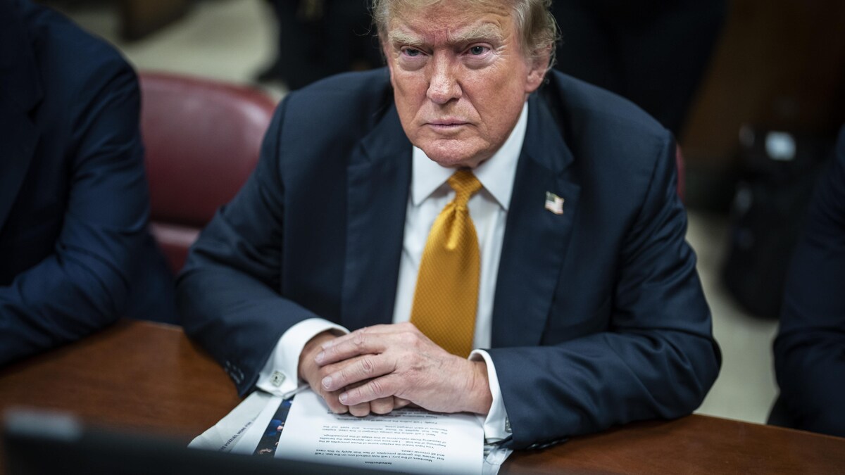 L'ancien président américain Donald Trump assis à une table avec en main des documents. 