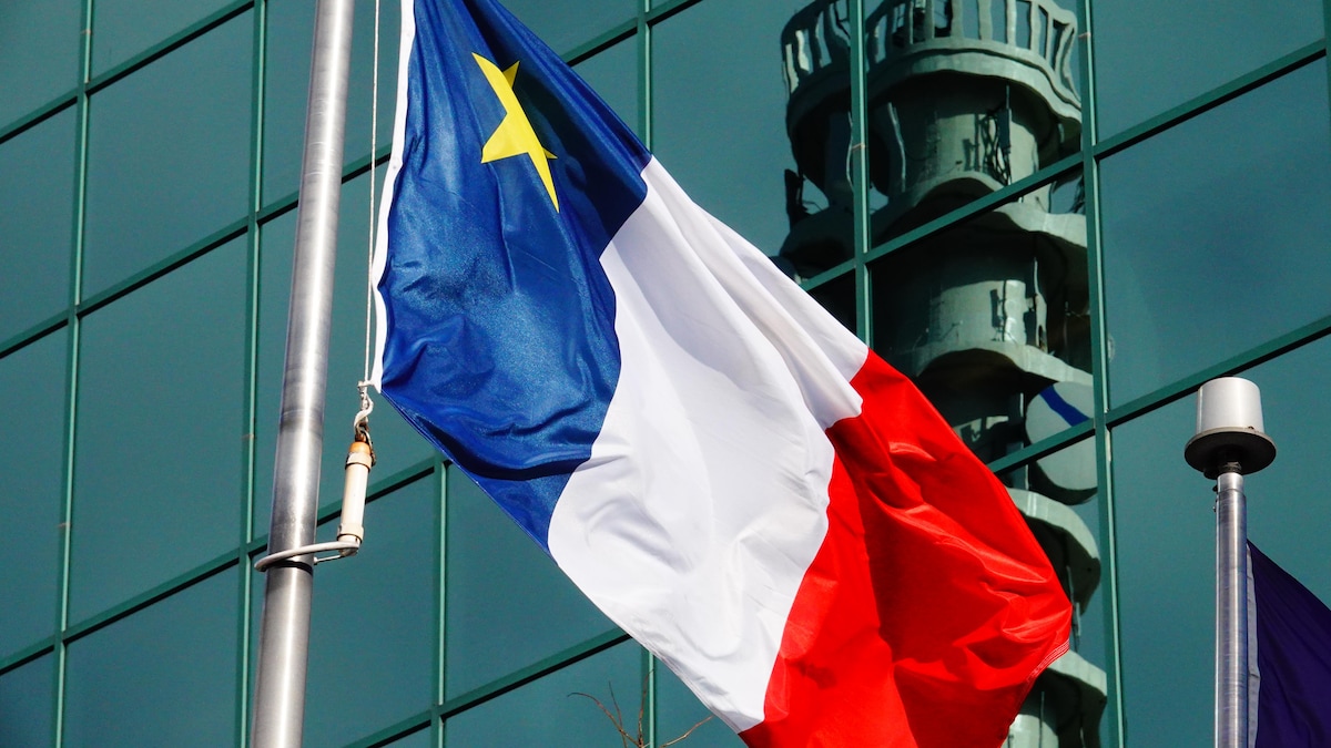 Drapeau acadien devant un édifice sur lequel est réfléchie la tour de Bell Aliant de Moncton.