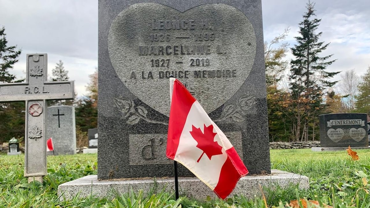 Un drapeau canadien est planté devant une pierre tombale.