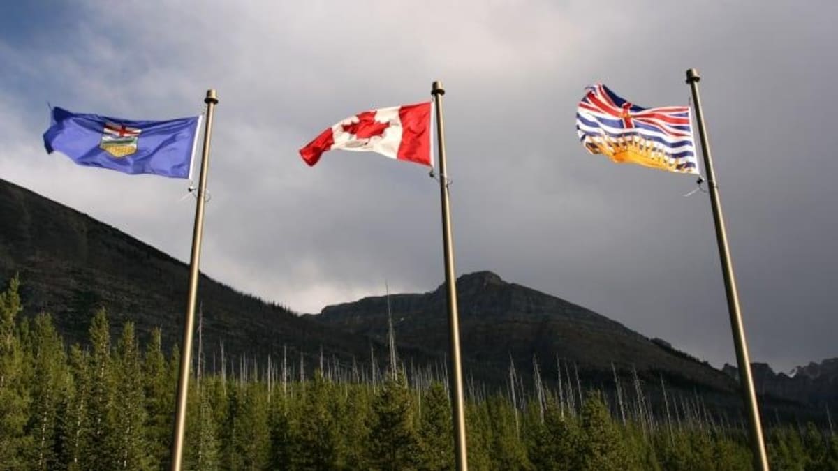 Trois drapeaux côte à côte dans le vent : un de l'Alberta, un du Canada et un de la Colombie-Britannique.