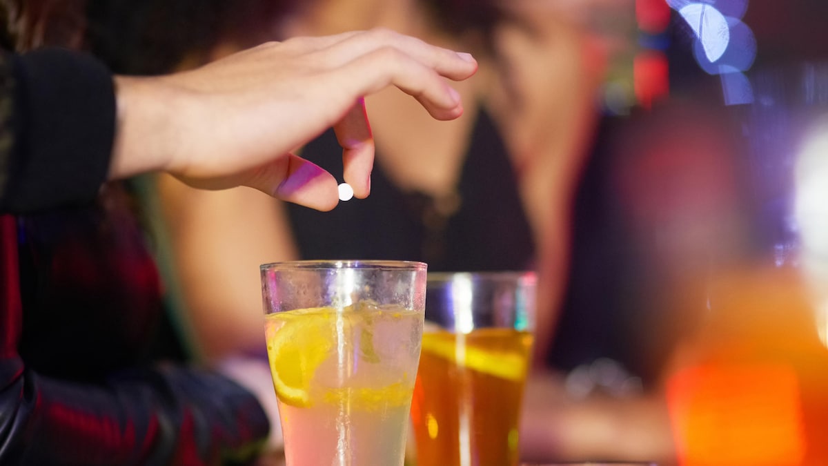 Gros plan sur la main d'un homme qui dépose une pilule blanche dans un cocktail, dans un bar. 