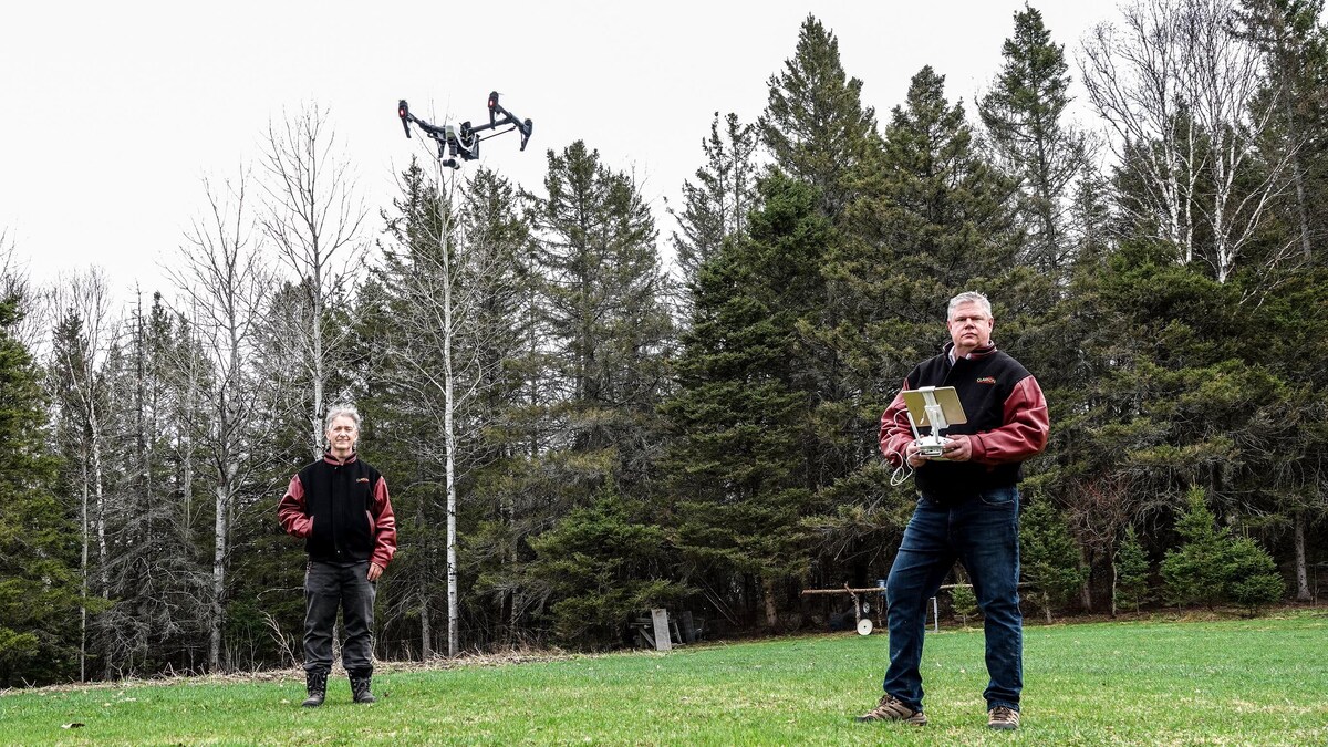 Bruce MacPherson et Darren Clarke une télécommande à la main sont debout alors qu'un drone vole au dessus de leur têtes.