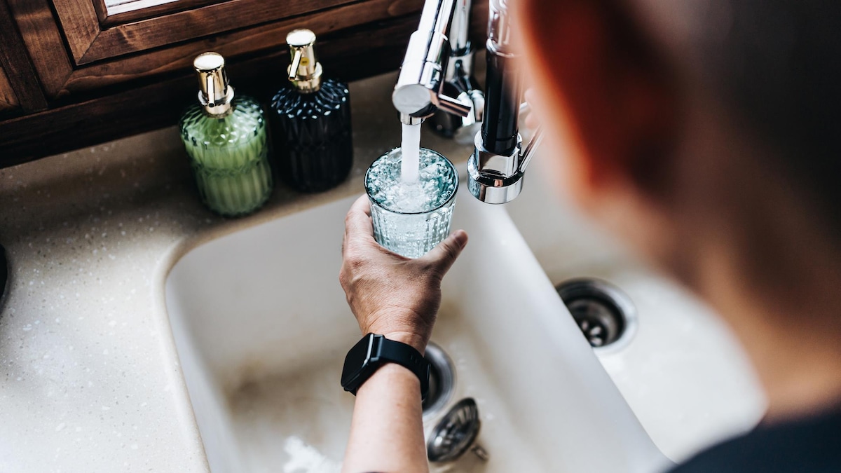 Un homme remplit un verre d'eau au robinet d'une cuisine.