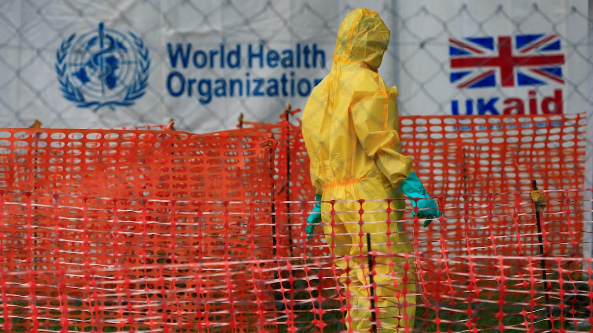 Une personne, vêtue d'une combinaison protectrice, se trouve devant une tente de l'Organisation mondiale de la santé.