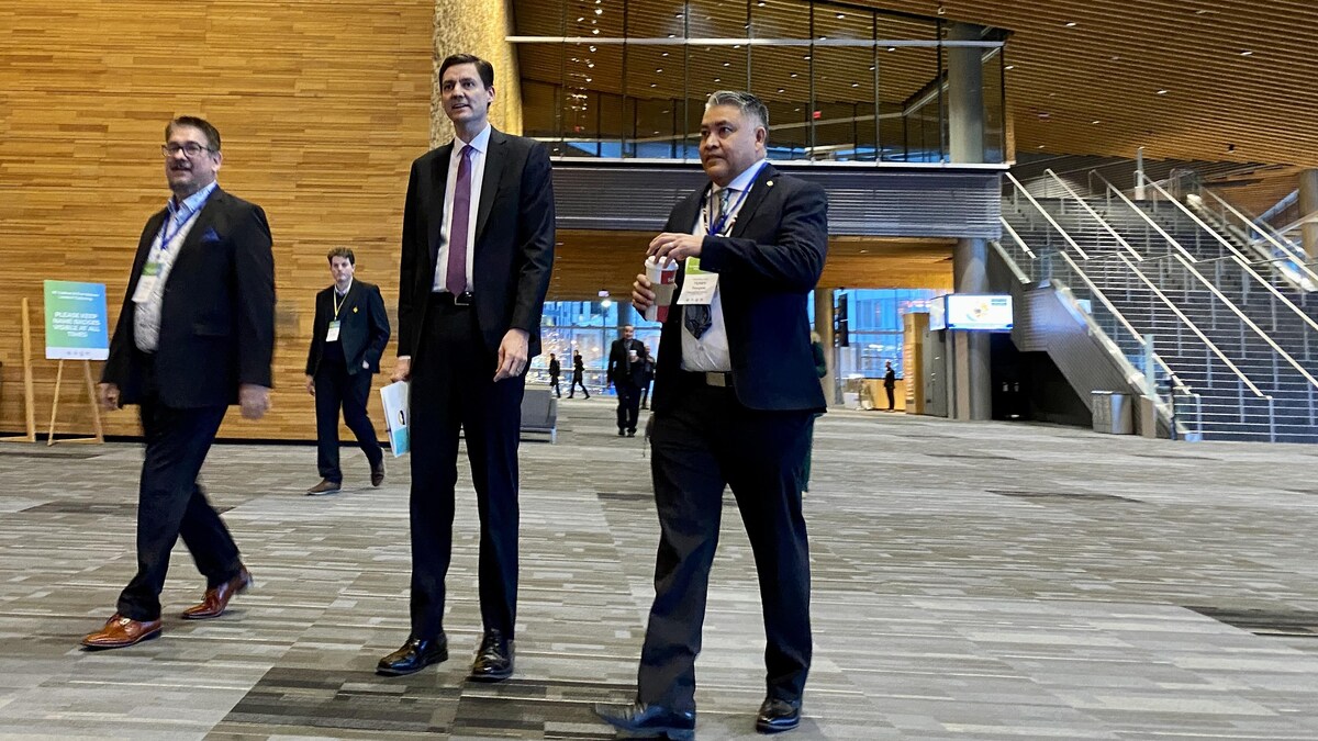 Trois hommes, dont David Eby et Robert Phillips, dans le grand hall du palais des congrès de Vancouver le 29 novembre 2022.