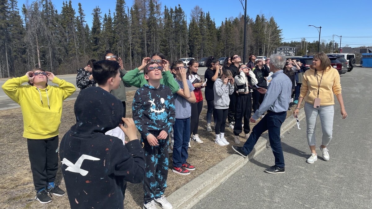 Des élèves et des enseignants sont rassemblés à l'extérieur et regardent vers le ciel avec des lunettes protectrices.