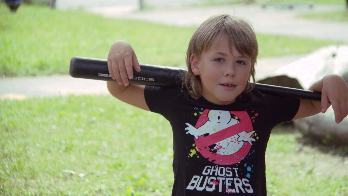 L'enfant tient dans son dos une batte de baseball.