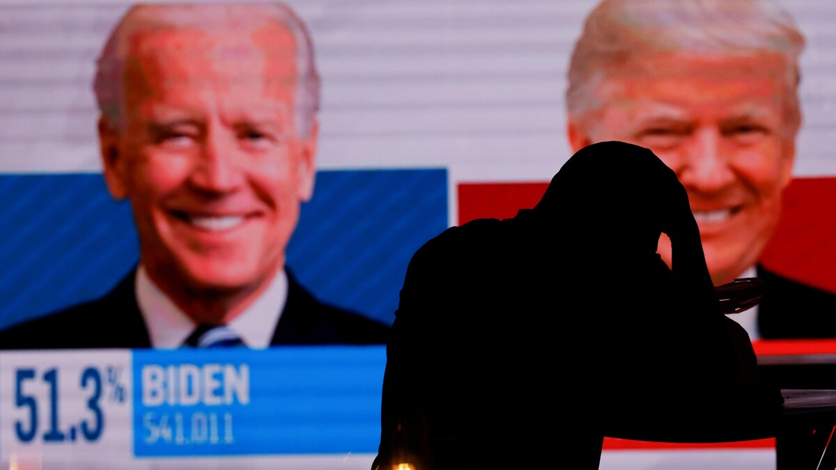 Une personne semble découragée devant un écran où sont affichés les portraits de Donald Trump et de Joe Biden.