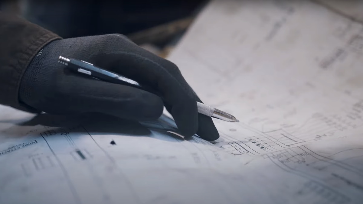 Une main tient un crayon sur un plan.