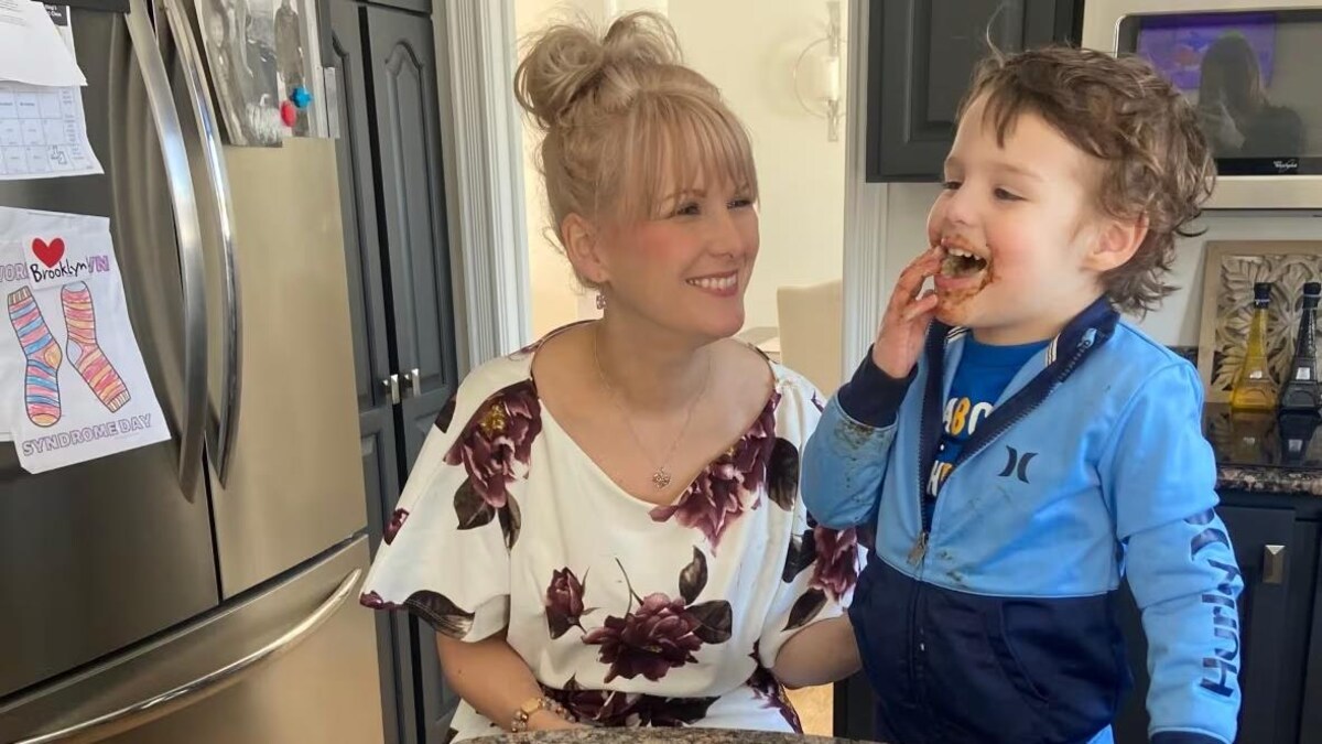 Une femme souriante regarde son fils manger son repas.