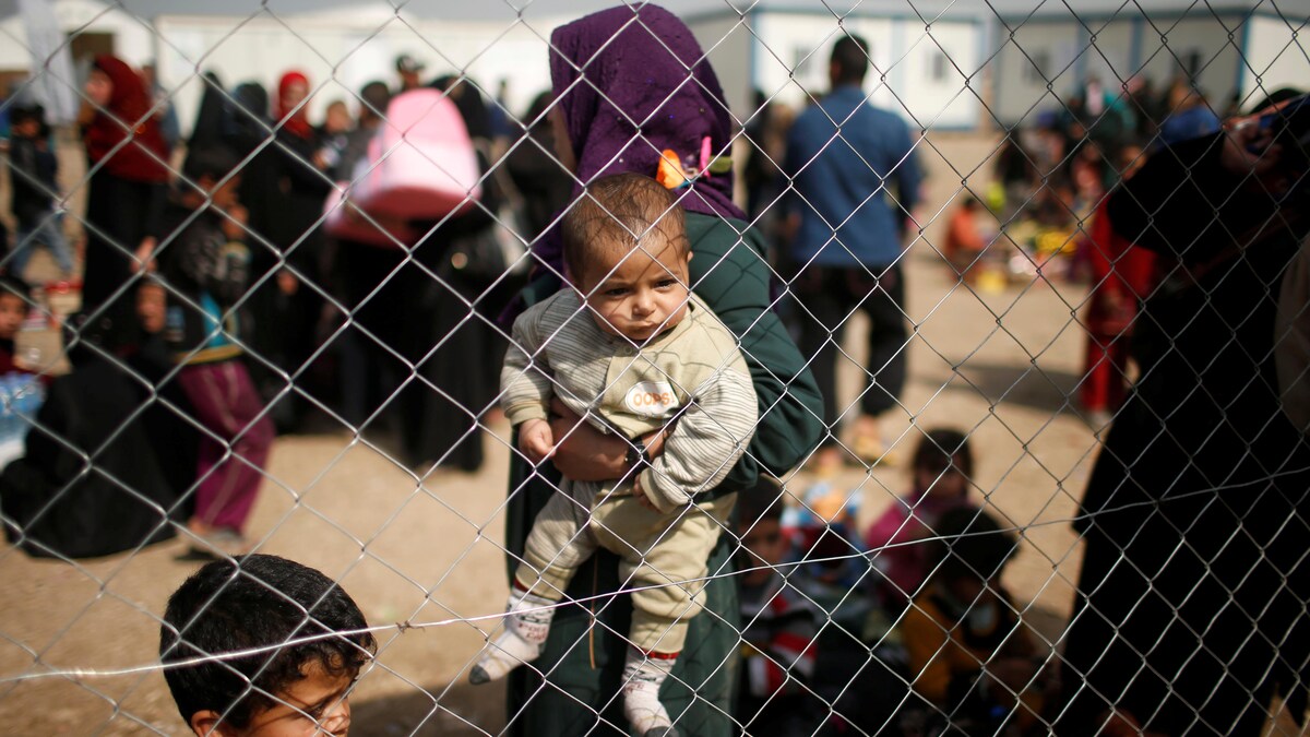 Des expatriés irakiens, photographiés derrière une clôture. Un enfant, dans les bras de sa mère, regarde la clôture.