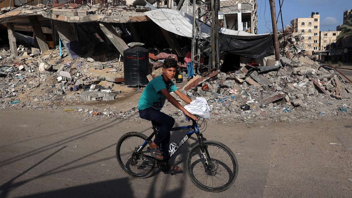 Un garçon passe à vélo devant un bâtiment détruit.