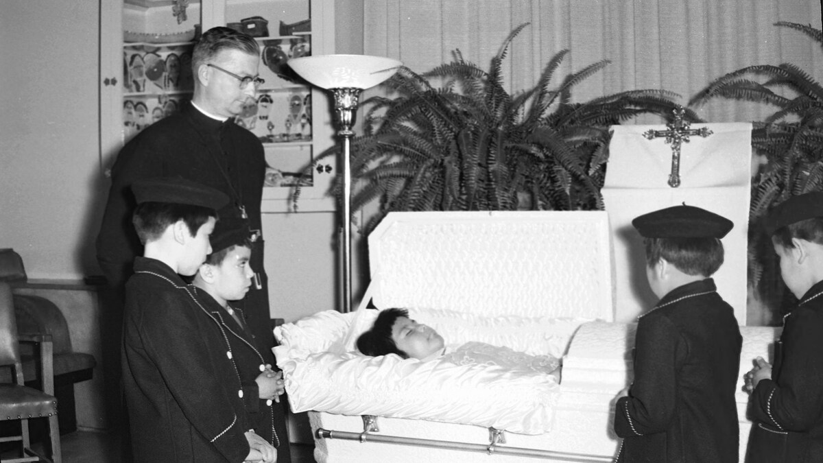 Des enfants et un prêtre devant la dépouille d'une enfant.
